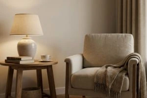 Cozy reading corner with a beige armchair and a warm ceramic table lamp on a wooden side table.